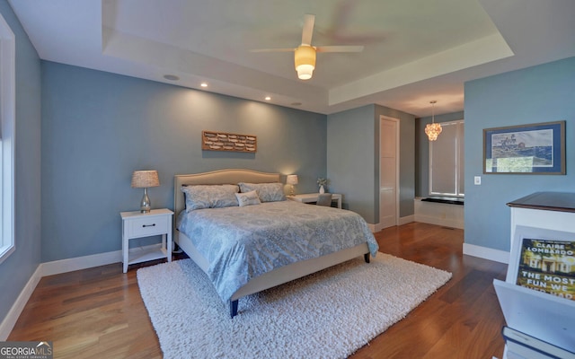 bedroom with dark wood-type flooring, ceiling fan, and a raised ceiling