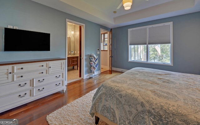 bedroom with ceiling fan, ensuite bath, light hardwood / wood-style flooring, and a tray ceiling