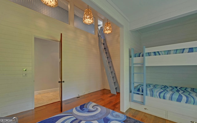 bedroom with wooden walls, an inviting chandelier, hardwood / wood-style flooring, and crown molding