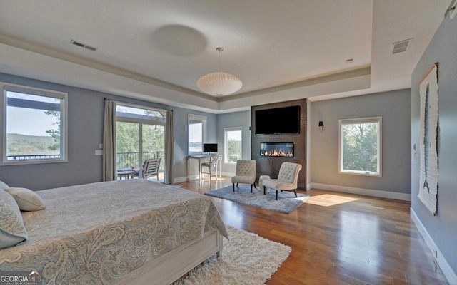 bedroom with wood-type flooring, a raised ceiling, and a fireplace