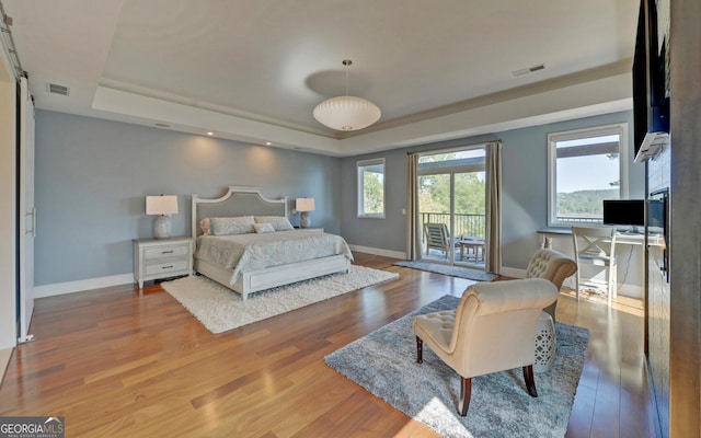 bedroom featuring hardwood / wood-style flooring, a raised ceiling, and access to outside