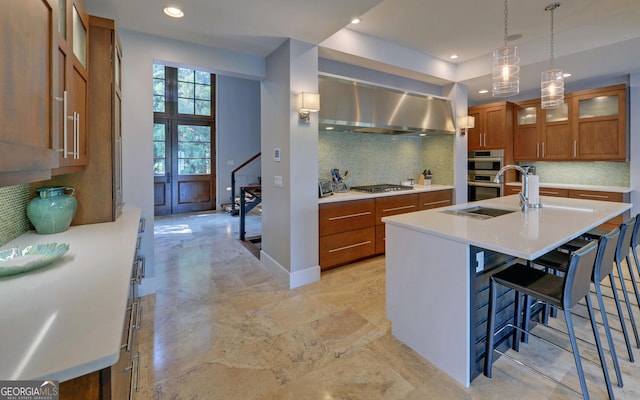 kitchen with stainless steel appliances, wall chimney exhaust hood, tasteful backsplash, an island with sink, and a breakfast bar