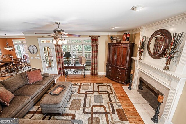 living room featuring ornamental molding, a tiled fireplace, ceiling fan, and light hardwood / wood-style flooring