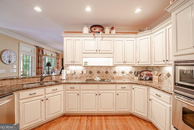 kitchen with stainless steel appliances, sink, dark stone counters, light hardwood / wood-style flooring, and ornamental molding