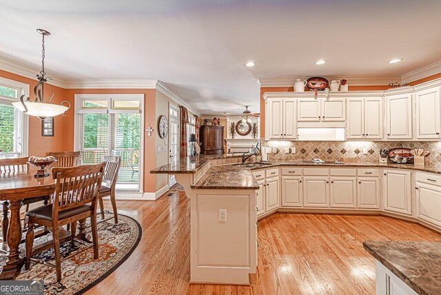 kitchen with dark stone counters, light hardwood / wood-style flooring, decorative light fixtures, kitchen peninsula, and ornamental molding