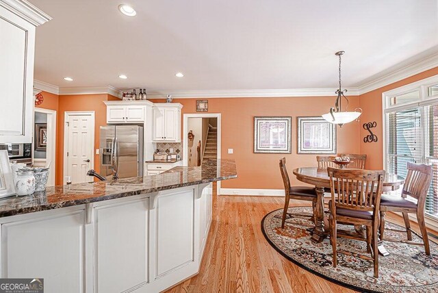 kitchen featuring light wood-type flooring, dark stone counters, stainless steel appliances, hanging light fixtures, and white cabinetry