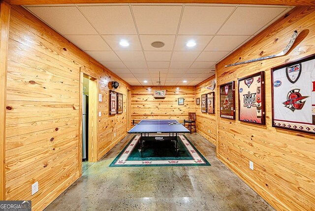 recreation room with a drop ceiling, wood walls, and a hot tub