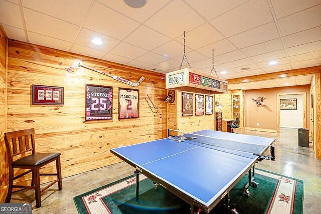 rec room with concrete flooring, wooden walls, and a paneled ceiling