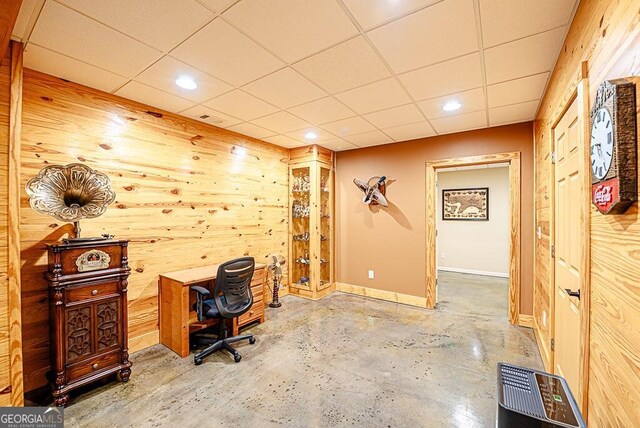 office area with concrete flooring, wood walls, and a paneled ceiling