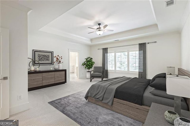 bedroom featuring light carpet, ceiling fan, ensuite bathroom, and a tray ceiling