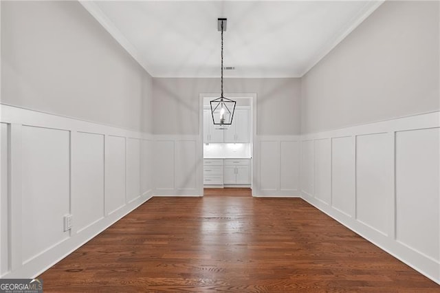 unfurnished dining area featuring ornamental molding, an inviting chandelier, and dark wood-type flooring