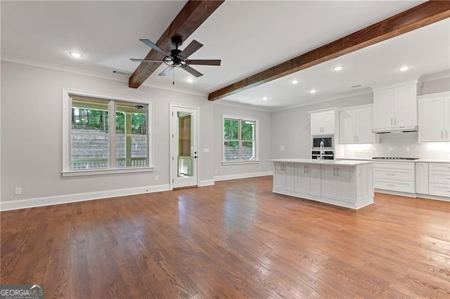 kitchen featuring white cabinets, beamed ceiling, a center island with sink, and a healthy amount of sunlight