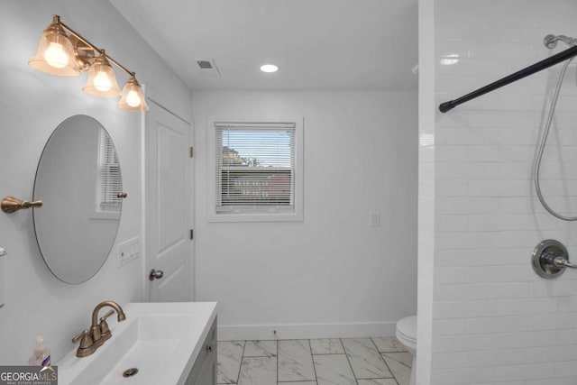 bathroom with tiled shower, vanity, and toilet