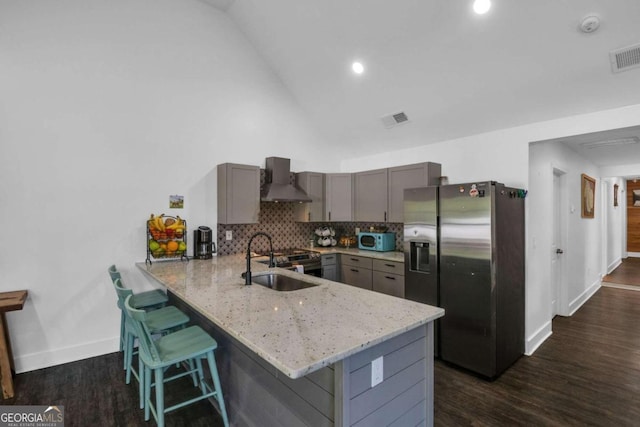 kitchen featuring sink, kitchen peninsula, stainless steel fridge with ice dispenser, wall chimney range hood, and a breakfast bar