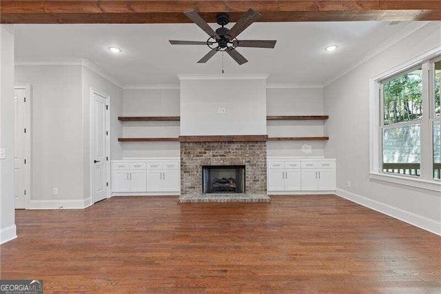 unfurnished living room with a brick fireplace, ceiling fan, beam ceiling, dark wood-type flooring, and ornamental molding