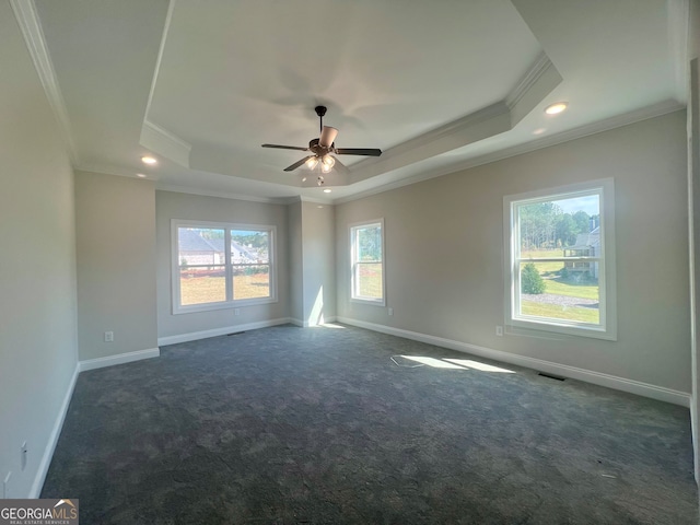 empty room with ornamental molding, ceiling fan, a tray ceiling, and dark carpet