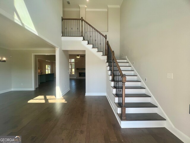 stairway featuring ornamental molding, hardwood / wood-style flooring, a brick fireplace, and a towering ceiling