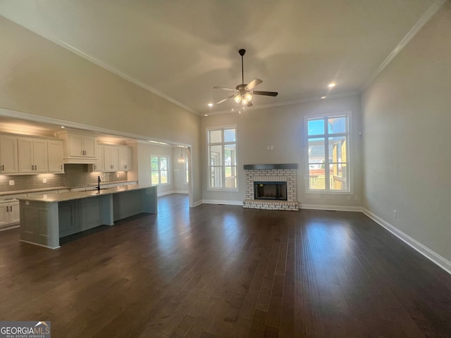 unfurnished living room featuring ceiling fan, sink, dark wood-type flooring, a fireplace, and crown molding