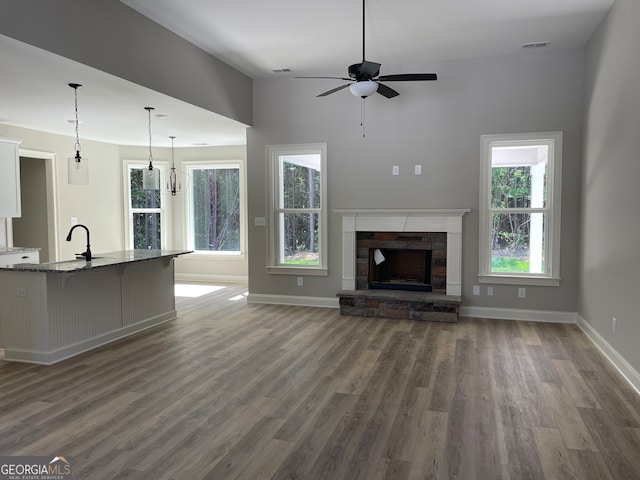 unfurnished living room with a fireplace, ceiling fan with notable chandelier, dark hardwood / wood-style flooring, and a healthy amount of sunlight