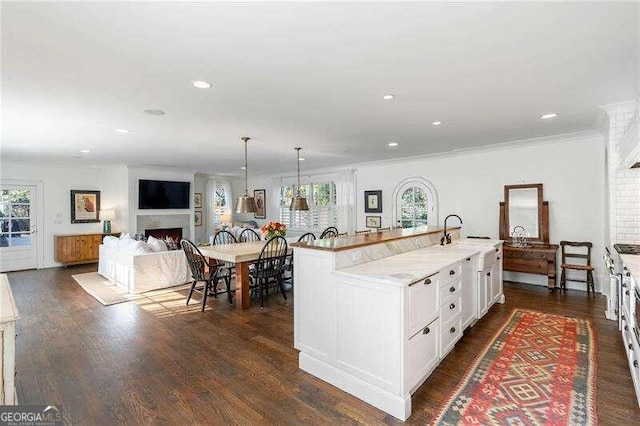 kitchen featuring dark wood-type flooring, a wealth of natural light, a kitchen island with sink, and decorative light fixtures