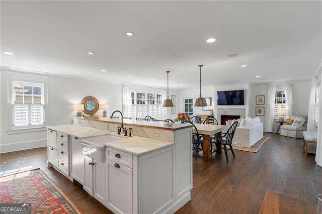 kitchen featuring dark hardwood / wood-style floors, sink, hanging light fixtures, an island with sink, and white cabinetry