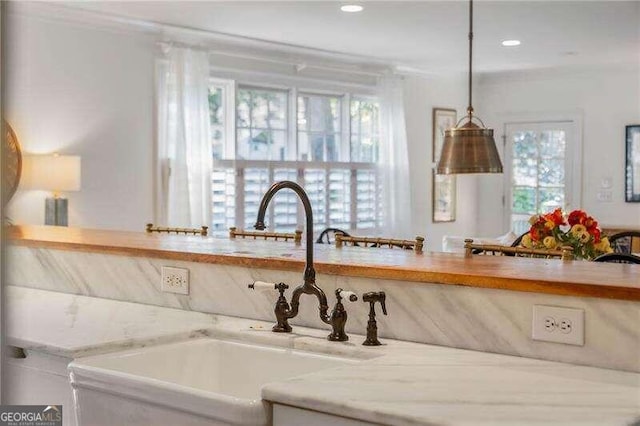 interior details with light stone countertops, ornamental molding, decorative light fixtures, and sink