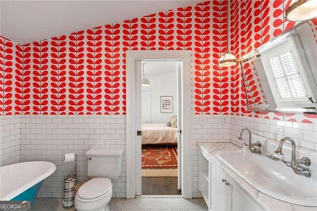 bathroom featuring toilet, tile walls, vaulted ceiling, a bathing tub, and vanity