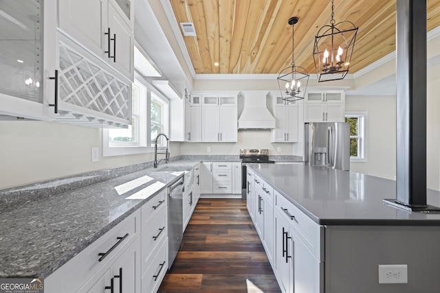 kitchen with custom range hood, decorative light fixtures, white cabinets, appliances with stainless steel finishes, and a center island