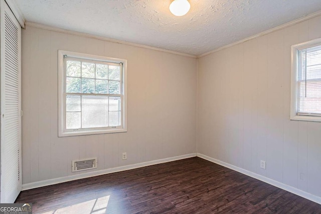 empty room featuring a textured ceiling, dark hardwood / wood-style flooring, a wealth of natural light, and crown molding