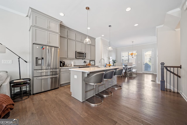 kitchen featuring pendant lighting, a center island with sink, dark wood-type flooring, gray cabinets, and stainless steel appliances