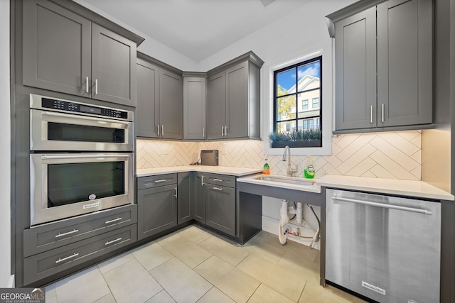 kitchen with gray cabinetry, tasteful backsplash, sink, stainless steel appliances, and light tile patterned floors