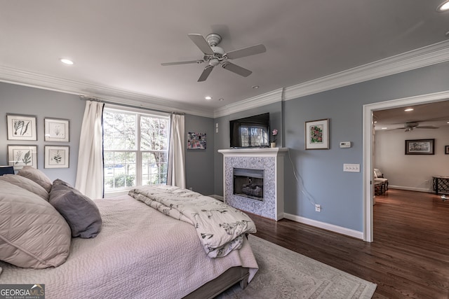 bedroom with ceiling fan, crown molding, dark wood-type flooring, and a tiled fireplace