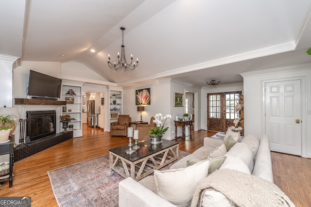 living room with a notable chandelier, vaulted ceiling, ornamental molding, and light hardwood / wood-style flooring