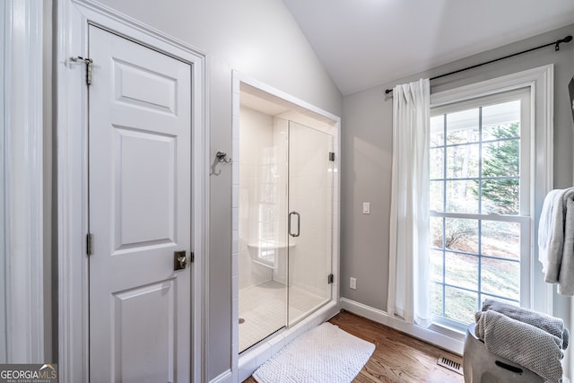 bathroom with plenty of natural light, wood-type flooring, vaulted ceiling, and walk in shower