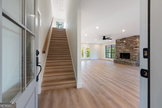 stairs featuring a stone fireplace, wood-type flooring, and ceiling fan