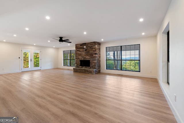 unfurnished living room featuring french doors, a stone fireplace, light hardwood / wood-style floors, and ceiling fan