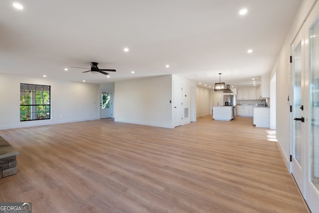 unfurnished living room with sink, light hardwood / wood-style flooring, and ceiling fan with notable chandelier