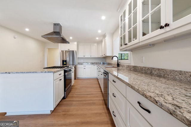 kitchen with wall chimney range hood, appliances with stainless steel finishes, white cabinetry, light hardwood / wood-style floors, and sink