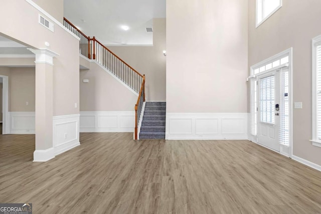 entrance foyer featuring a high ceiling, decorative columns, crown molding, and light hardwood / wood-style floors