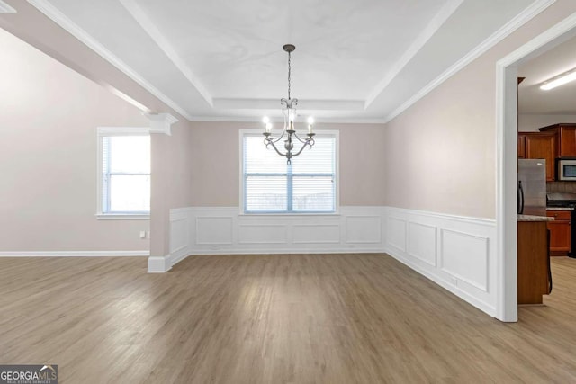 unfurnished dining area featuring light wood-type flooring, a raised ceiling, ornate columns, a chandelier, and ornamental molding