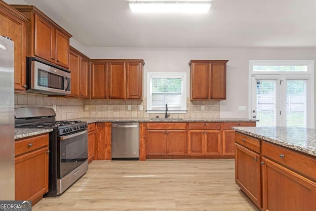 kitchen featuring light stone counters, stainless steel appliances, light wood-type flooring, and sink