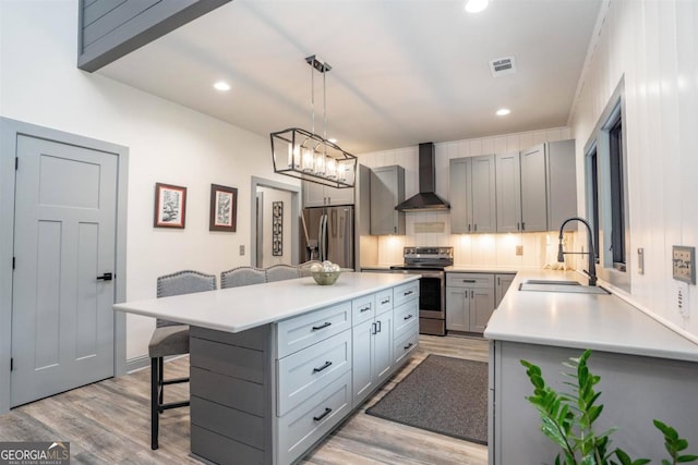 kitchen with wall chimney range hood, a breakfast bar, decorative light fixtures, sink, and stainless steel appliances