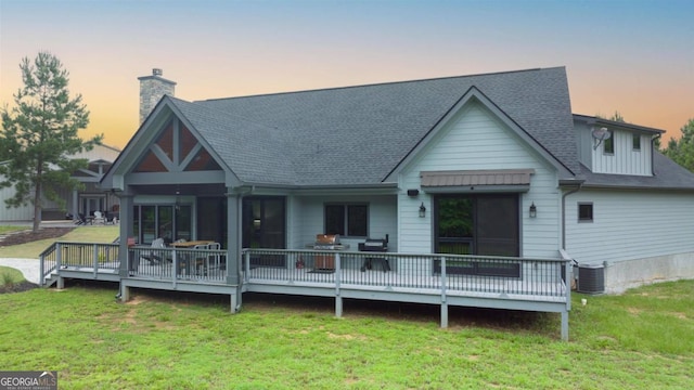 back house at dusk with a wooden deck, central AC unit, and a lawn