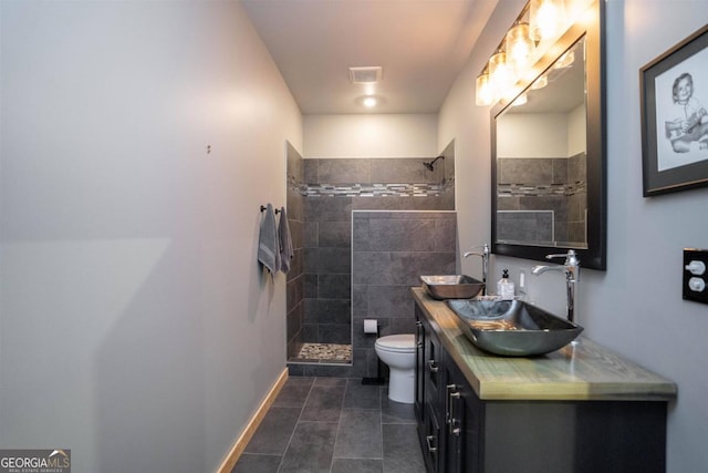 bathroom with tile patterned flooring, tiled shower, vanity, and toilet