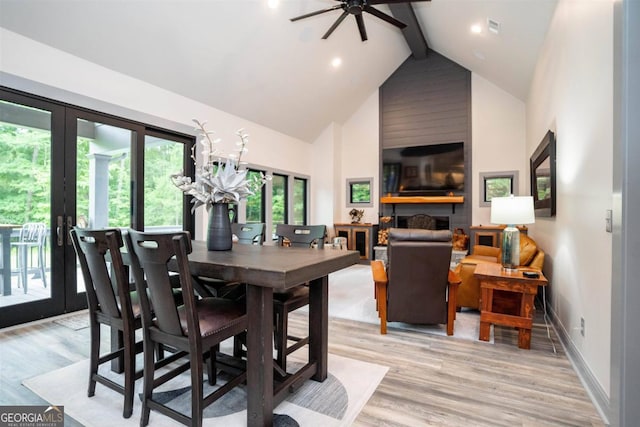 dining space featuring light wood-type flooring, high vaulted ceiling, ceiling fan, beamed ceiling, and a large fireplace