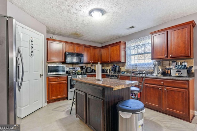 kitchen featuring appliances with stainless steel finishes, a kitchen island, a breakfast bar area, and a textured ceiling