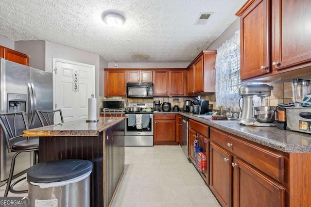 kitchen with a kitchen bar, sink, stainless steel appliances, and a textured ceiling