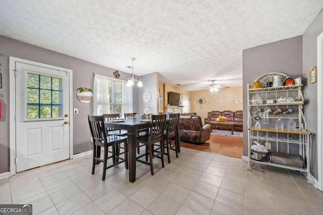 tiled dining area featuring a textured ceiling and ceiling fan with notable chandelier