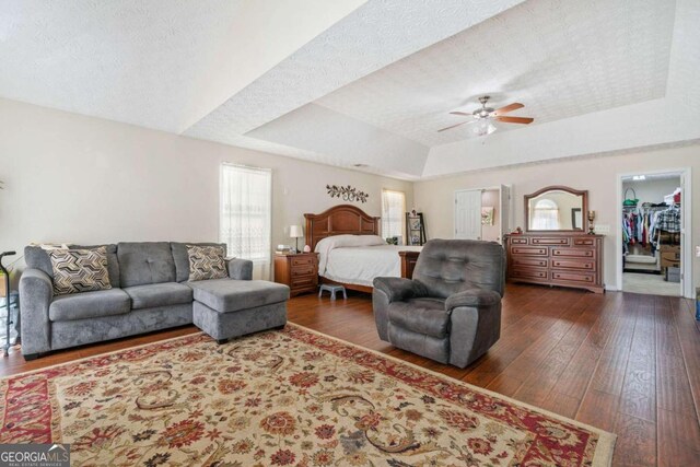 bedroom featuring ceiling fan, dark hardwood / wood-style flooring, a tray ceiling, a walk in closet, and a textured ceiling