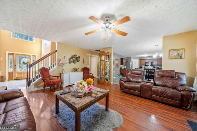 living room featuring ceiling fan with notable chandelier, hardwood / wood-style floors, and a textured ceiling